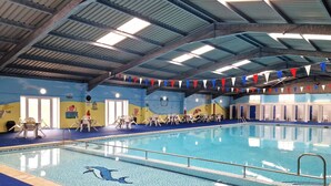 Une piscine intérieure aux couleurs bleu et blanc, entourée de chaises longues et ornée d’une fresque représentant une scène de plage.