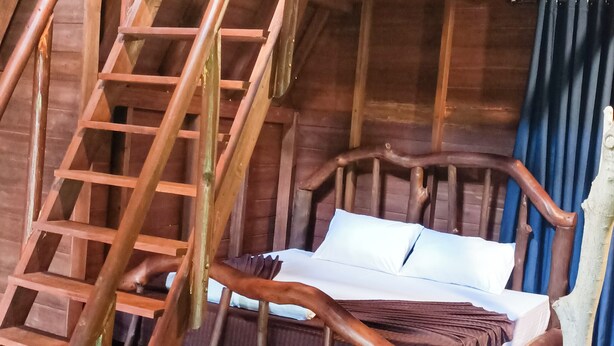 Una escalera de madera que lleva a un dormitorio en un altillo con una cama y un ventanal.