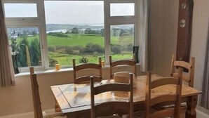 A dining area with a wooden table and chairs, large windows with a view of green fields. - 3-bedroom house in Killybegs with WiFi perfect for kids and family (Killybegs)