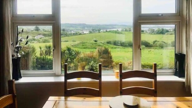 A dining area with a table and chairs facing a large window with a view of green fields and hills. - 3-bedroom house in Killybegs with WiFi perfect for kids and family (Killybegs)