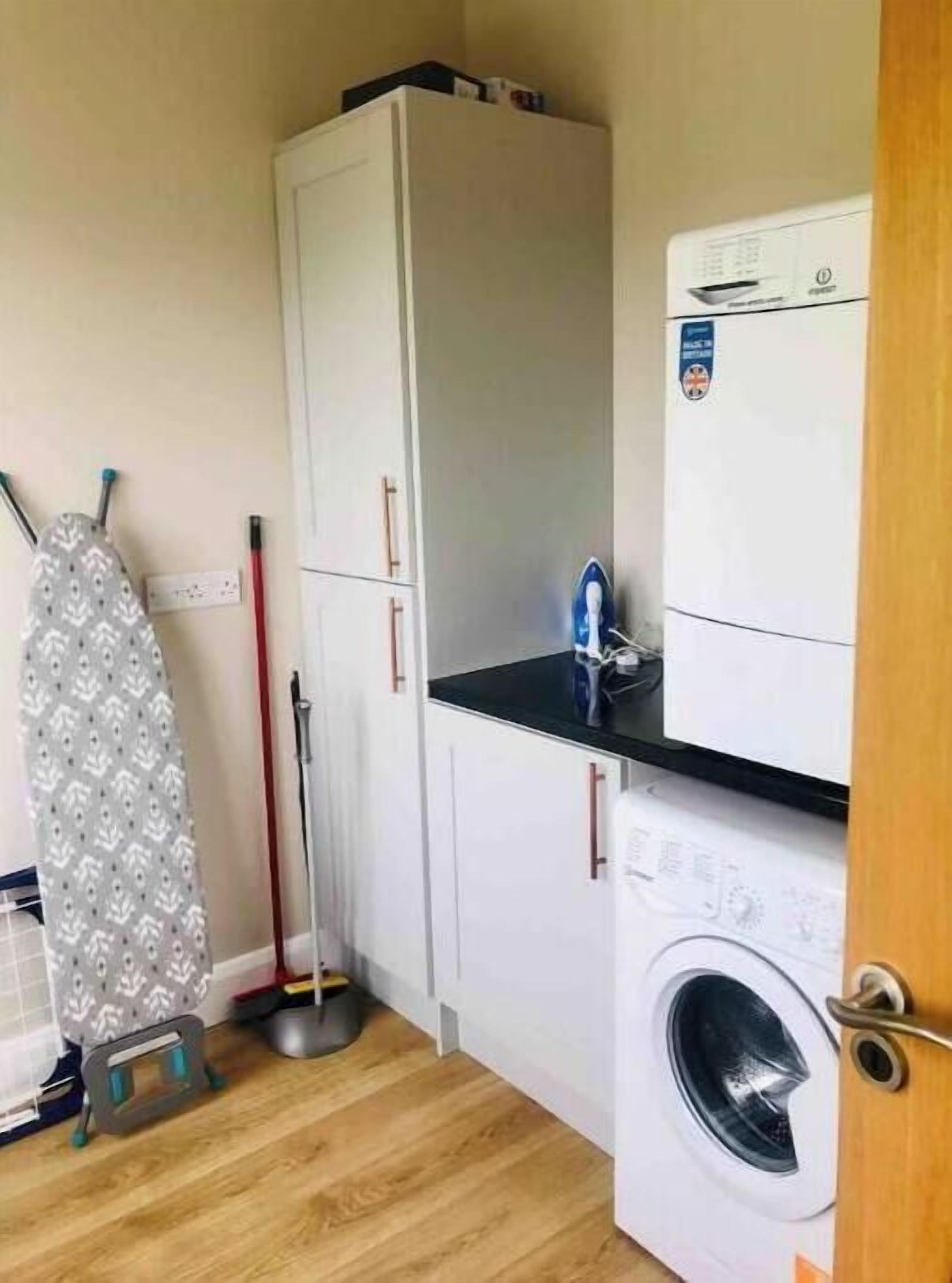 A compact laundry room with a washing machine, a drying rack, and a broom.