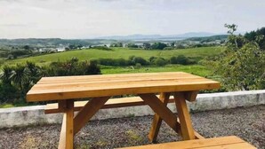 A wooden picnic table with a view of a green landscape and distant hills. - 3-bedroom house in Killybegs with WiFi perfect for kids and family (Killybegs)
