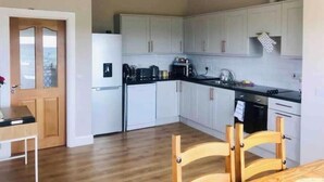 A modern kitchen with white cabinets, a black countertop, and a wooden dining table with chairs. - 3-bedroom house in Killybegs with WiFi perfect for kids and family (Killybegs)