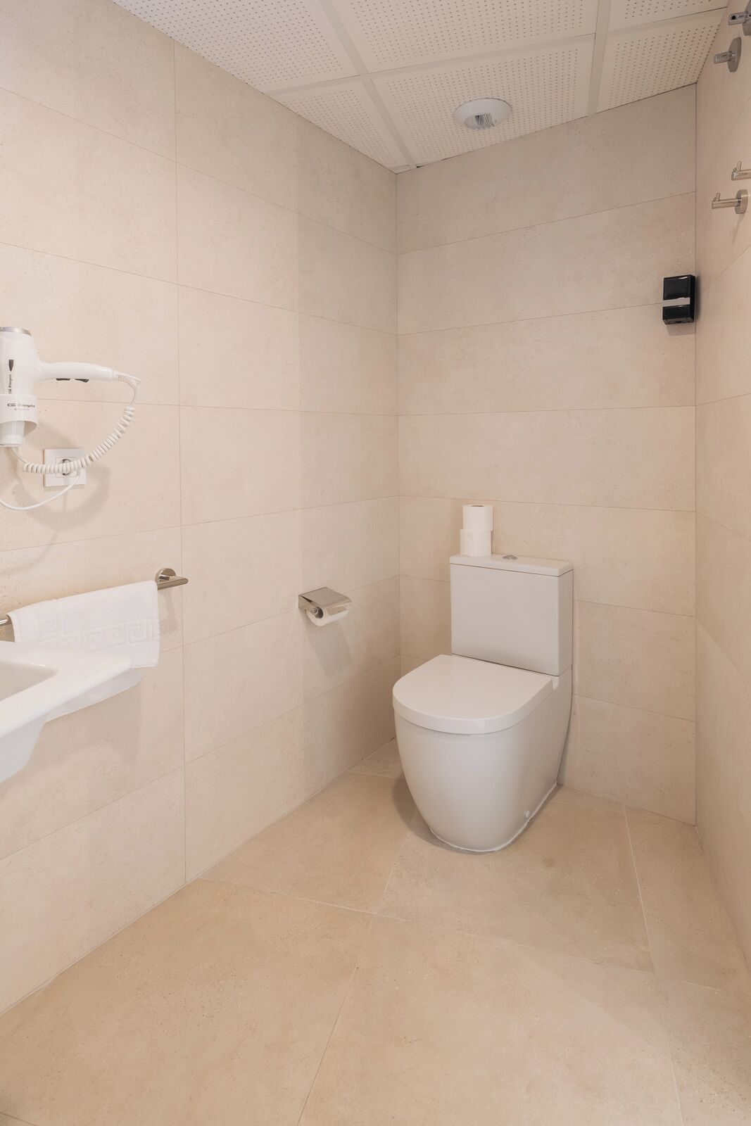 A small, modern bathroom with a toilet, a sink, and a hairdryer mounted on the wall.