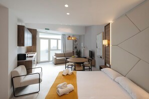 A hotel room with a bed, a sofa, a dining table, a TV, and a bathroom with a shower. - MARINA AZURA (Valencia)