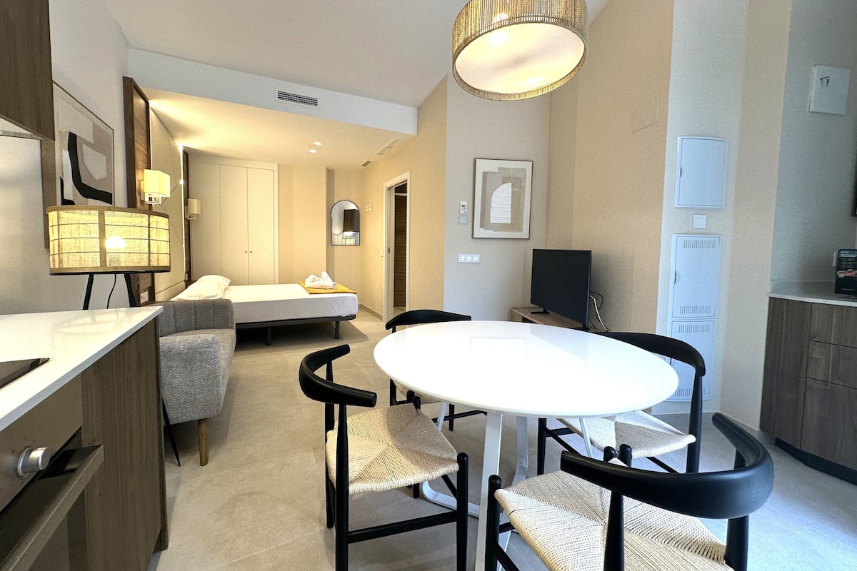 A modern hotel room with a bed, a desk, a chair, a round table, and a television.