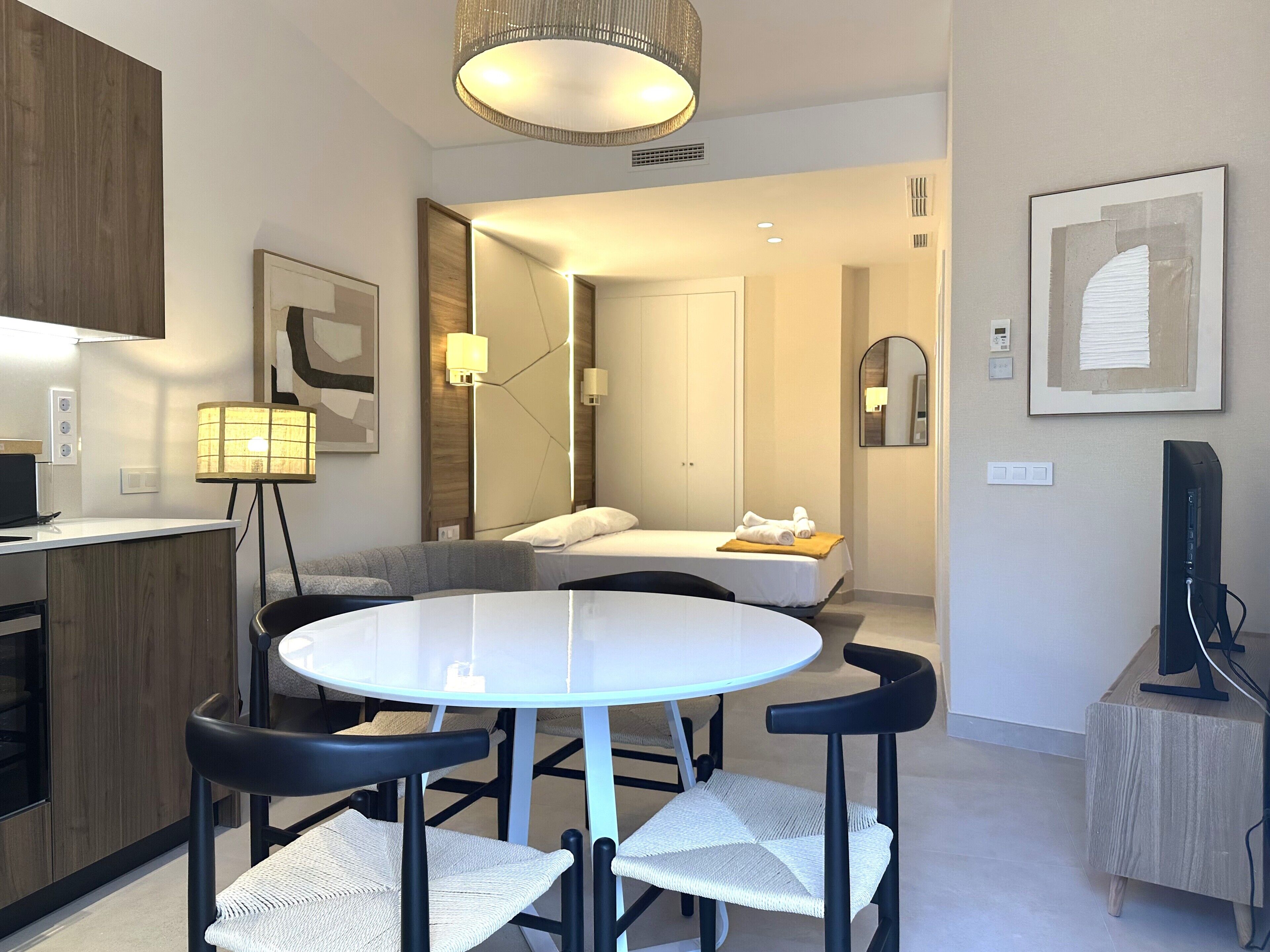 Una habitación de hotel moderna con una mesa de comedor redonda, dos sillas, una cama, un televisor y una kitchenette.