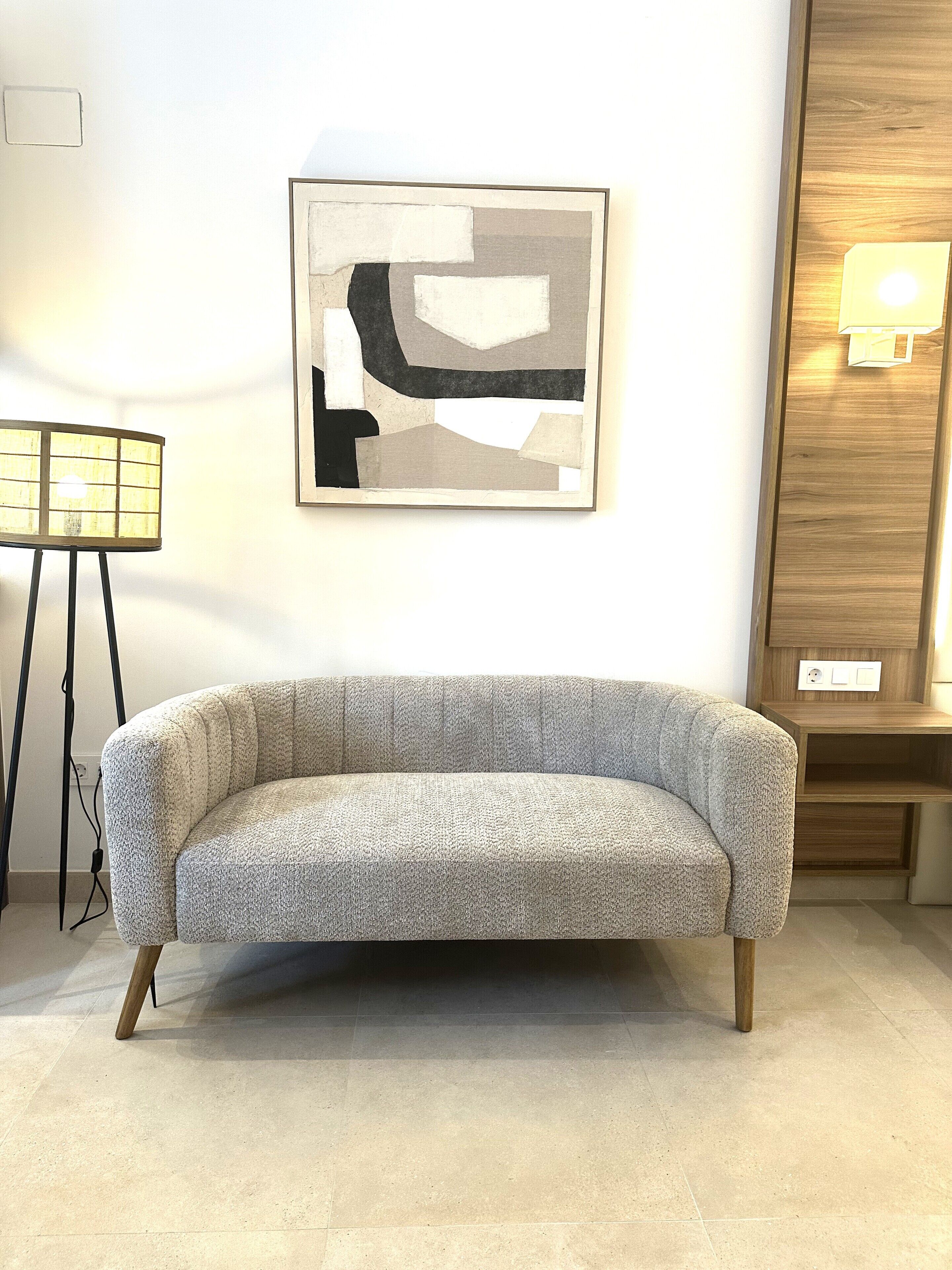 Una sala de estar moderna con un sofá gris, un cuadro abstracto enmarcado y un mueble de madera con luz.