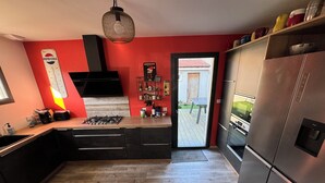 Eine moderne Küche mit roter Akzentwand, einem Gasherd, einem Edelstahlkühlschrank und einem Holzboden im Fischgrätmuster.