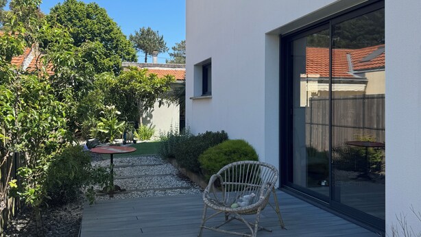 Ein modernes Haus mit Terrasse, einem Korbstuhl und einem Kiesweg.