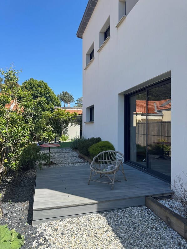 Ein modernes Haus mit Terrasse, einem Korbstuhl und einem Kiesweg.