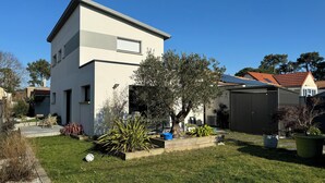 Ein modernes, zweistöckiges Haus mit gepflegtem Rasen, einer Terrasse mit Gartenmöbeln und einem großen Baum.