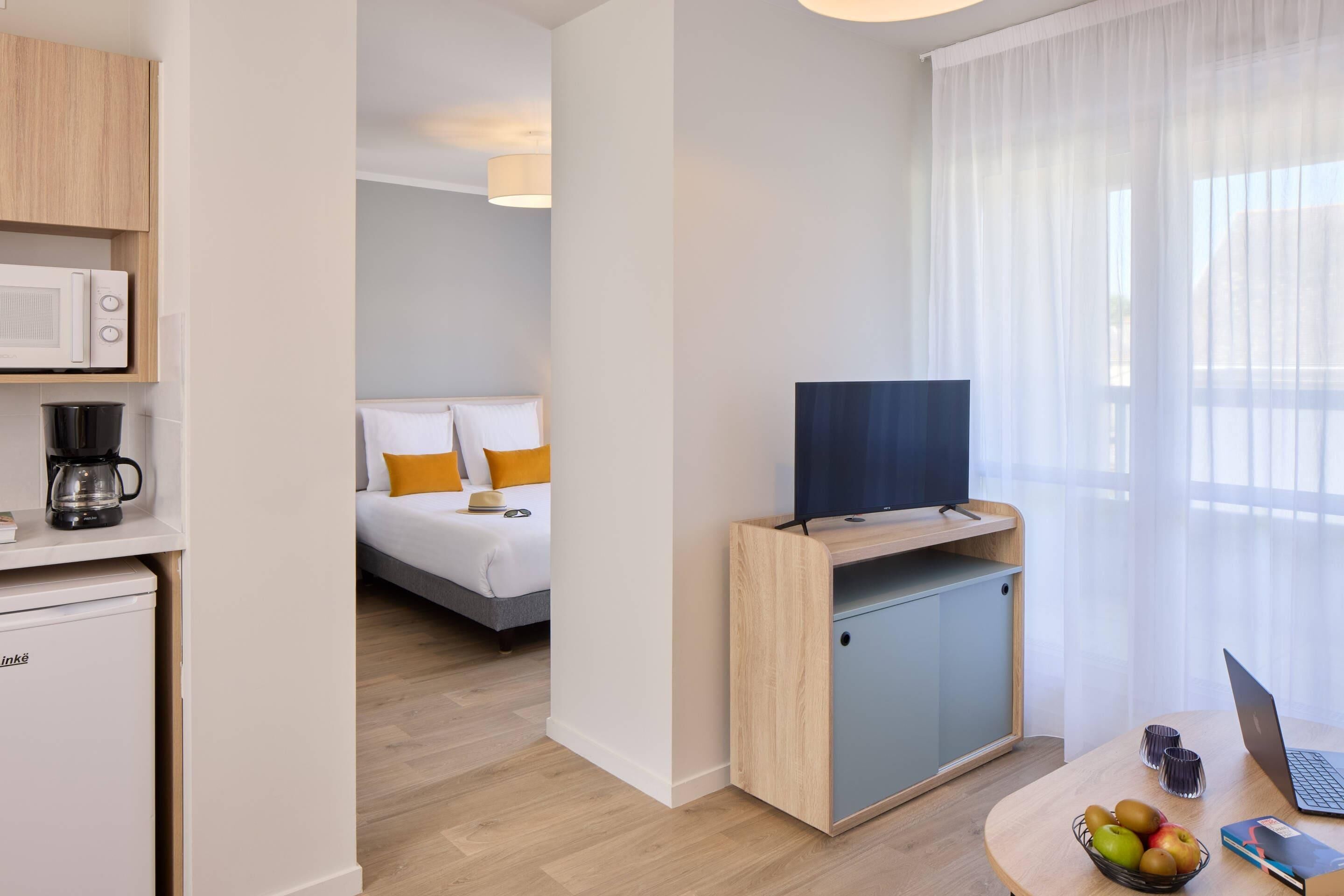 Une chambre d’hôtel moderne équipée d’un lit, d’une télévision, d’un bureau avec un ordinateur portable, d’une machine à café et d’un mini-réfrigérateur.