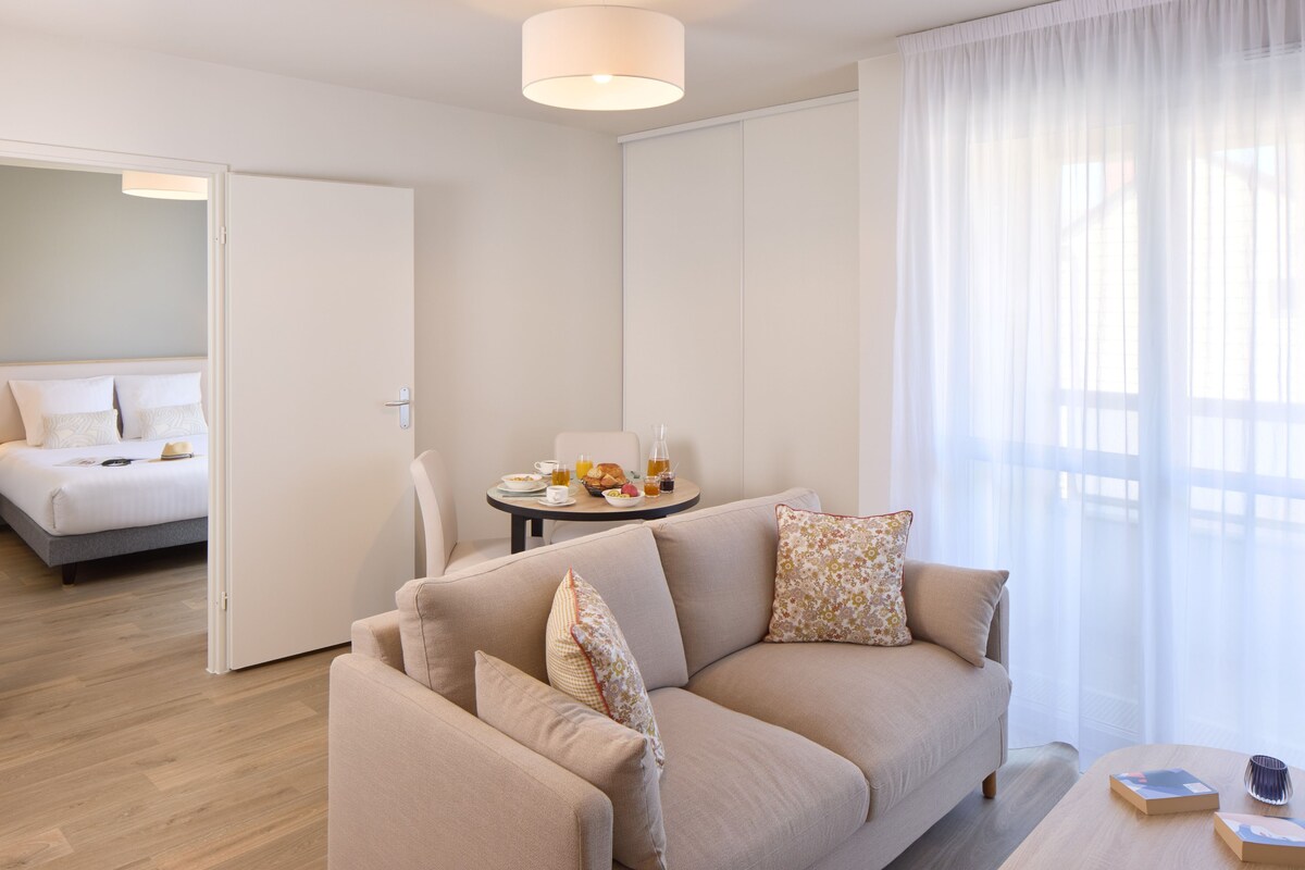 Ein modernes Wohnzimmer mit einer Couch, einem Esstisch mit Frühstücksgebäck und einem Bett im Hintergrund.
