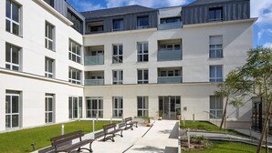 A modern multi-story building with a courtyard featuring benches and potted plants. - Quality Aparthotel Saumur (Saumur)