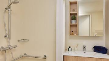 A modern bathroom with a shower, a sink, a mirror, and a shelf with toiletries.