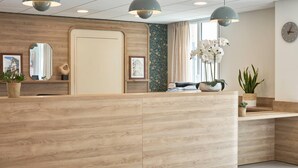 A reception area with a wooden reception desk, pendant lighting, framed pictures, and potted plants. - Quality Aparthotel Saumur (Saumur)