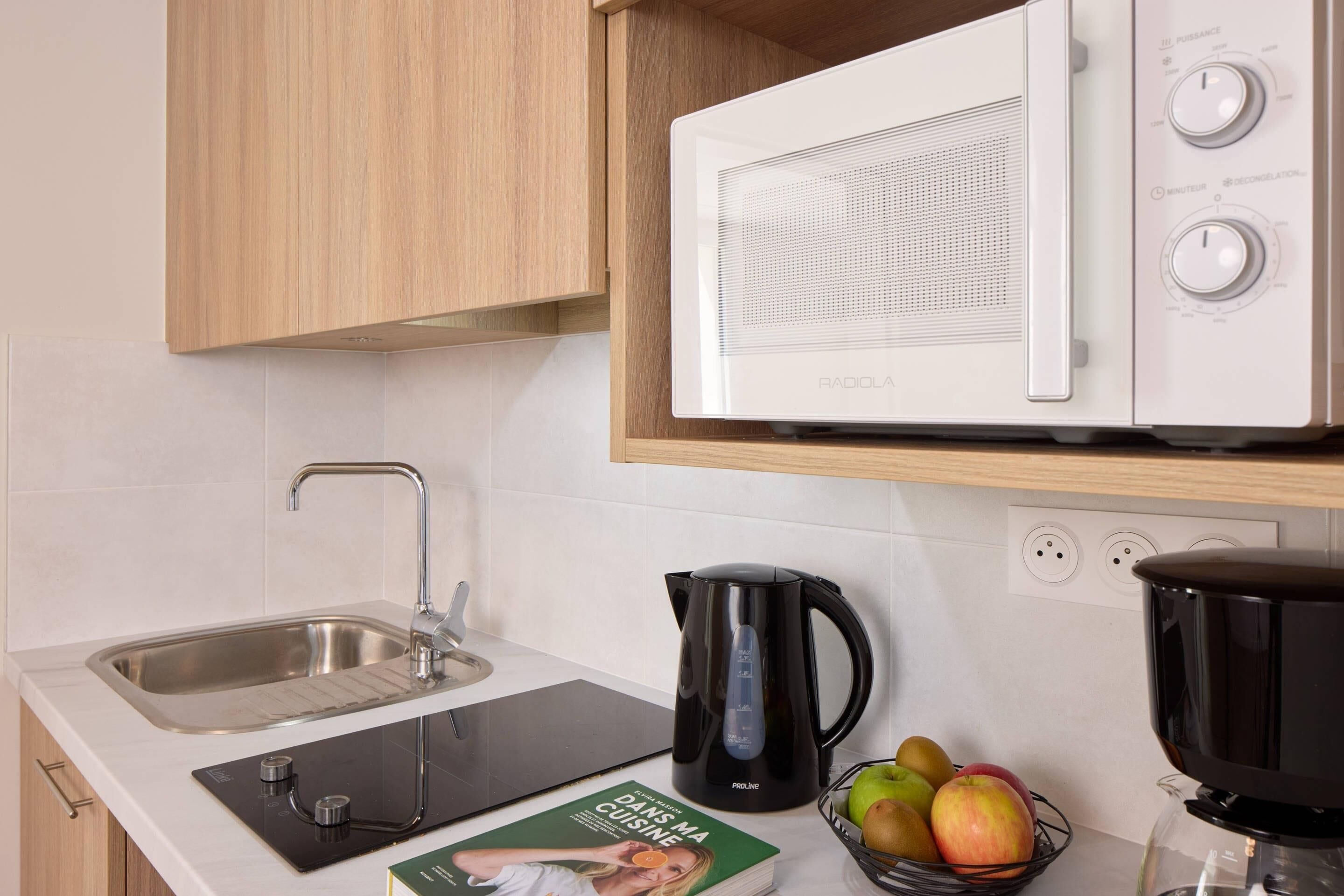 Una cocina con microondas, hervidor y un libro sobre la encimera.
