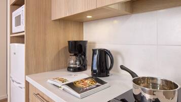 A kitchen with a microwave, coffee maker, kettle, and a cookbook on the counter.