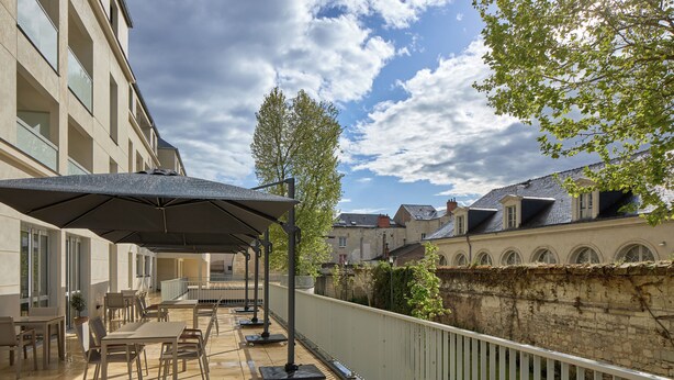 An outdoor patio with tables and chairs, a covered seating area, and a view of a stone wall and buildings in the background. - Quality Aparthotel Saumur (Saumur)
