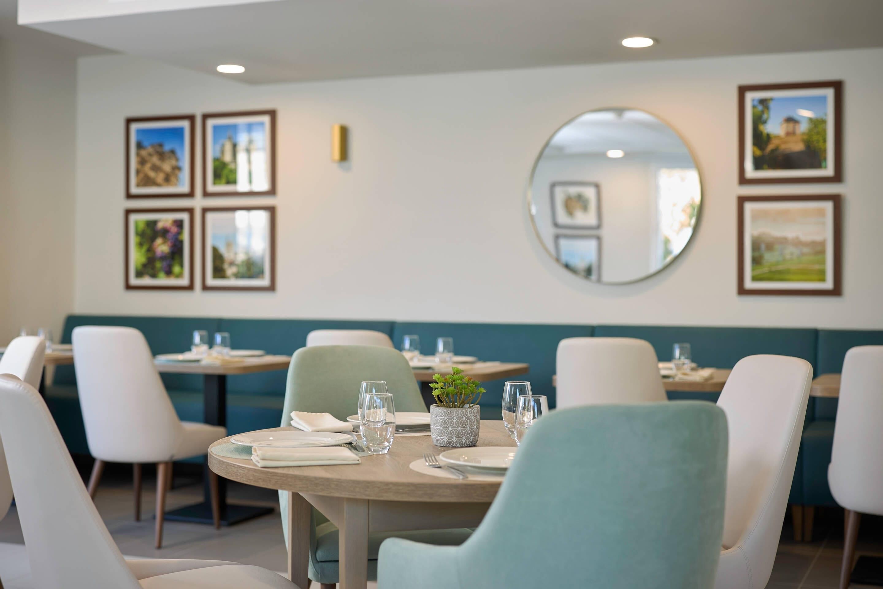 A restaurant with round tables, white chairs, and a green booth area.