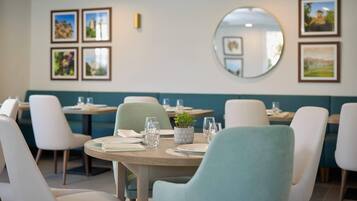 Un restaurant avec des tables rondes, des chaises blanches et un coin salon vert.