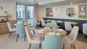 A modern dining area with round tables, white and teal chairs, and a wooden buffet. - Quality Aparthotel Saumur (Saumur)