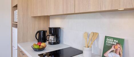Una cocina con armarios de madera, cafetera, tetera, un tazón de fruta, libro de cocina y utensilios de madera.