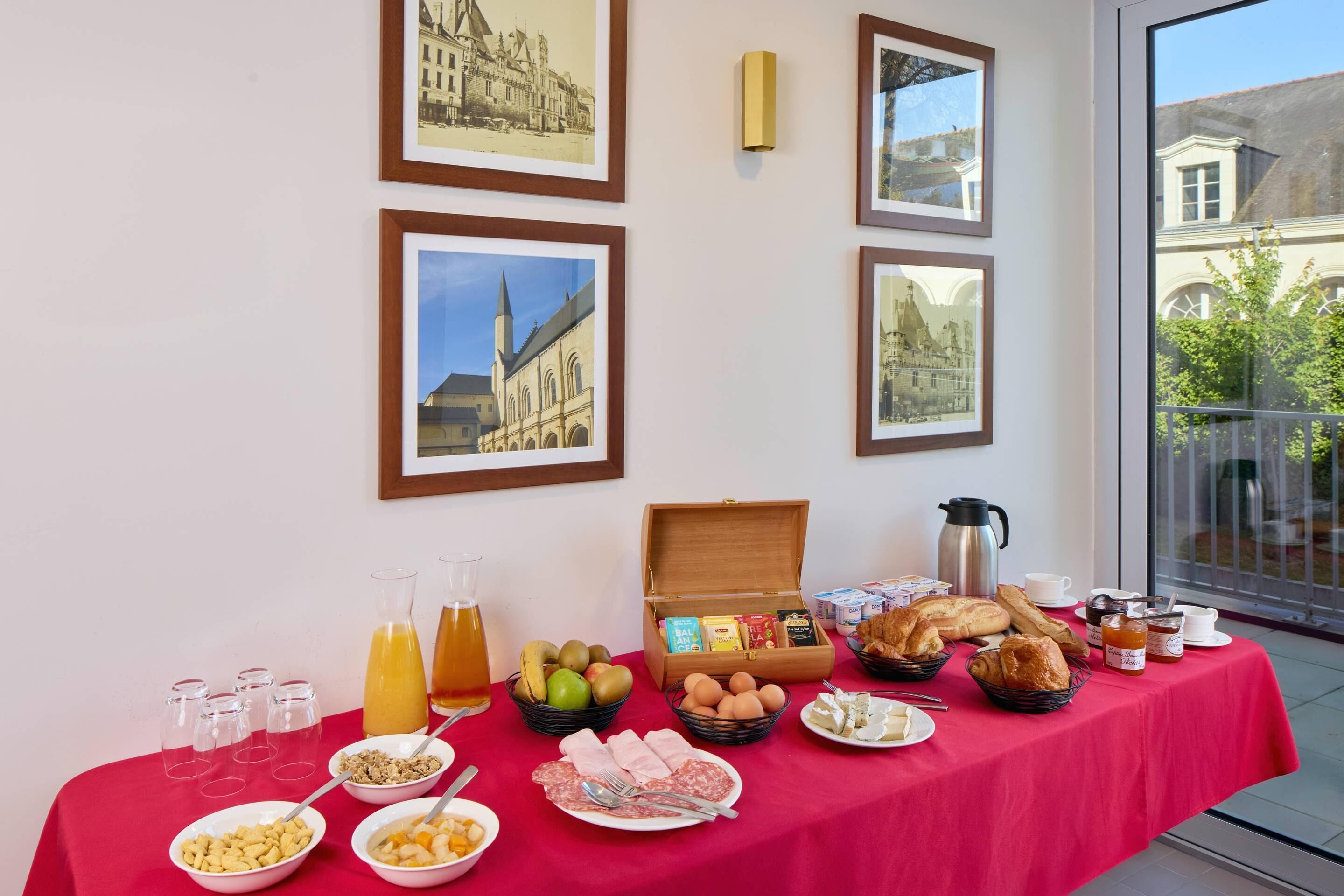 Un bufé de desayuno con diversos alimentos y una estación de café, cuadros en la pared y vistas de edificios a través de una ventana.