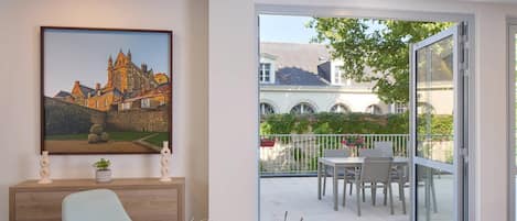 Un comedor con una mesa lista para el desayuno, un cuadro de un castillo en la pared y vista a un patio con un edificio al fondo.
