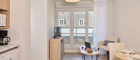 Una sala de estar moderna con comedor, una cocina equipada con cafetera y un ventanal con vistas a edificios.