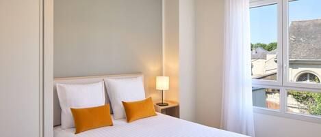 Una cama bien hecha con ropa de cama blanca y naranja, un sombrero, gafas de sol y una revista sobre la cama.