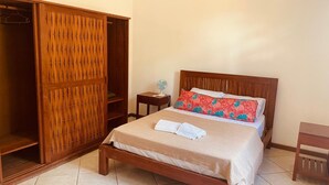 A bedroom with a wooden bed, a wardrobe, a bedside table with a lamp, and a small chair.
