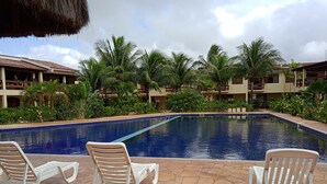 A swimming pool with lounge chairs, surrounded by palm trees and a building with a tiled roof.