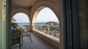 A balcony with a tiled floor, two chairs, a table with food, and a view of the sea through arches. - Elysium Living Parga (Parga)
