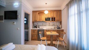A compact kitchen with wooden cabinets, a microwave, and a small dining area with two chairs. - Elysium Living Parga (Parga)