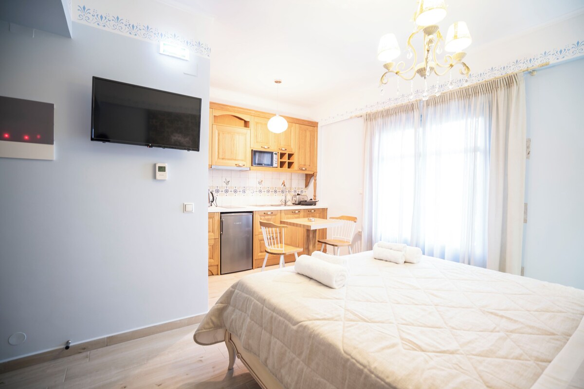 A hotel room with a bed, a TV, a kitchenette, and a dining area.