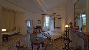 Et hotelværelse med himmelseng, siddeområde med bord og stole, et lille skrivebord og et spejl.