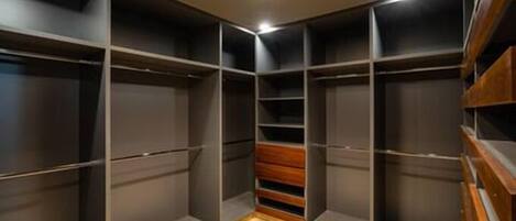 Un vestidor con amplias repisas y cajones, un banco de madera y una lámpara en el techo.