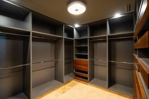 Ein begehbarer Kleiderschrank mit mehreren Regalen und Schubladen, einer Holzbank und einer Deckenleuchte.