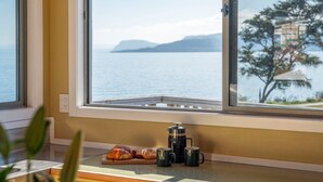 A kitchen with a view of a lake and mountains, a coffee maker, and a croissant on the counter.