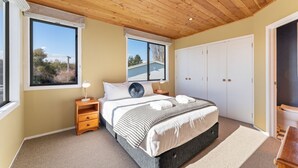 A bedroom with a bed, two bedside tables, a wardrobe, and large windows.