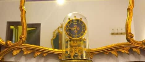 Ein Spiegel mit verziertem Goldrahmen, der einen Raum mit einer Kandelaber und einer Uhr reflektiert.