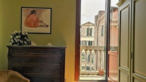 Une pièce avec une commode en bois, un tableau encadré accroché au mur et une vue sur une cour intérieure par une porte ouverte.