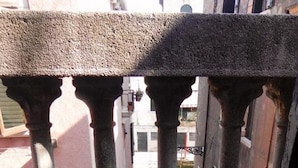 Un balcon doté de balustrades en pierre et offrant une vue sur une cour intérieure, avec des bâtiments en arrière-plan.