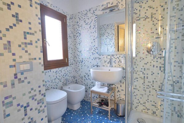A bathroom with mosaic tile walls, a white sink, a bidet, and a shower.