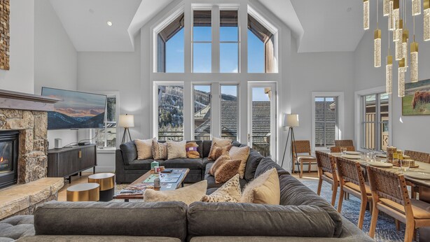 A spacious living room with a fireplace, large windows, a dining area, and a high ceiling. - Slopeside Townhome in Beaver Creek | Chalet Montsor (Beaver Creek)