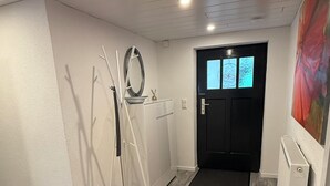 Un couloir moderne et bien éclairé, avec une porte noire, un radiateur blanc et un tapis rouge à motifs.