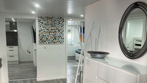 Un intérieur moderne avec un plancher en bois, un meuble blanc doté d’un miroir et un mur décoré d’une mosaïque colorée.