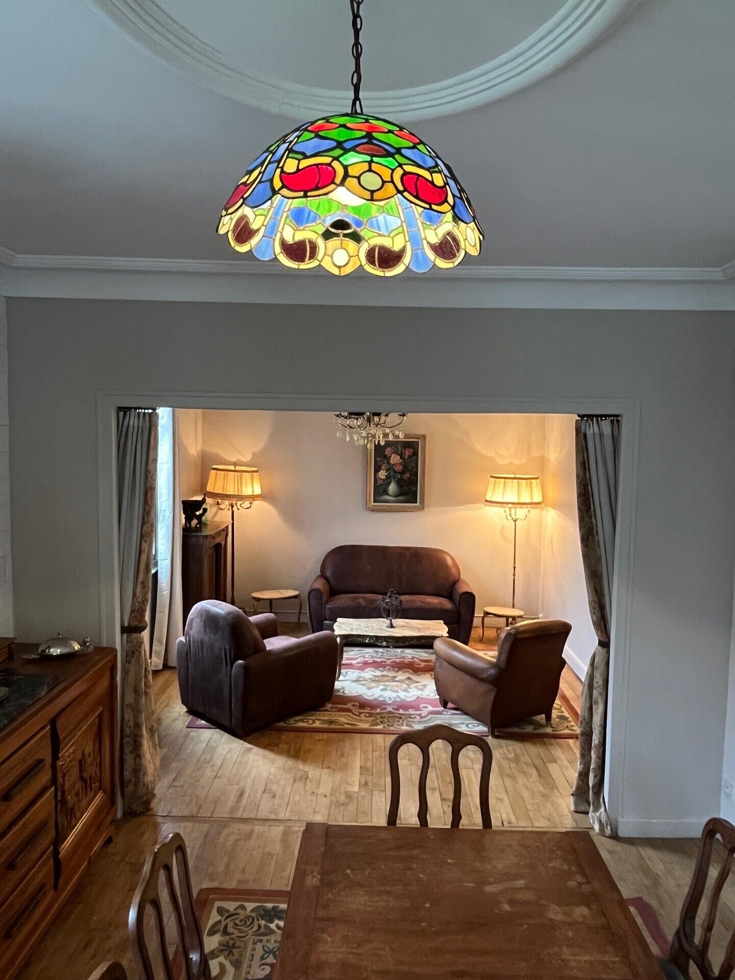 Een eethoek met een houten tafel en stoelen, een kroonluchter en een bank op de achtergrond.